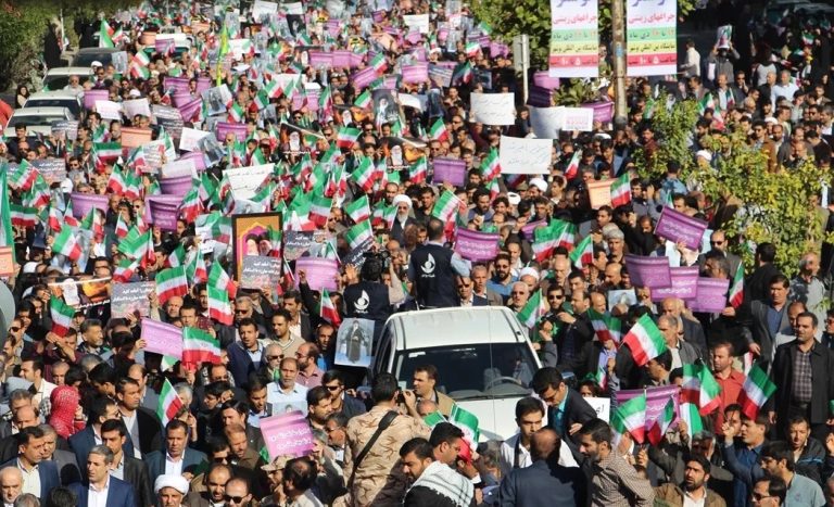Large crowd of Iranian protesters carrying national flags and portraits during a street demonstration.