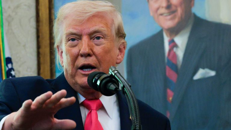 Donald Trump speaking at a microphone with a portrait of Ronald Reagan in the background.