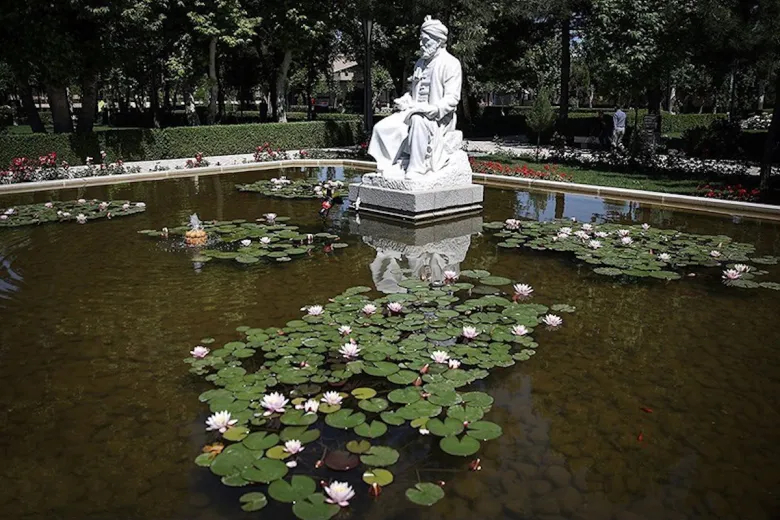 A white marble statue of a Persian scholar sitting by a reflective lily pond in a traditional Persian garden.