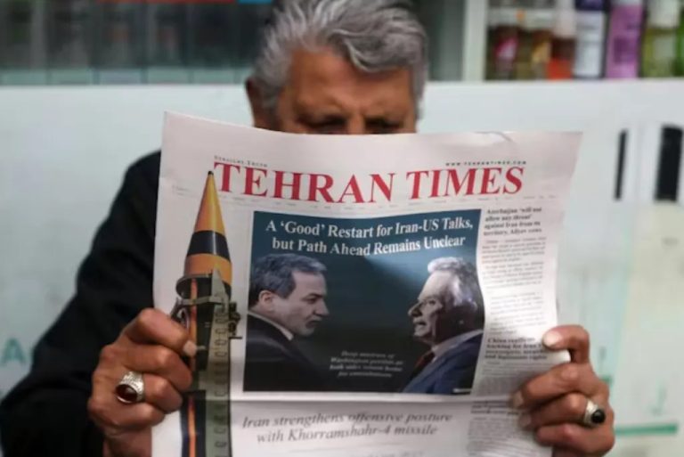 A person holding a Tehran Times newspaper featuring a headline about Iran-US talks and an image of a missile.