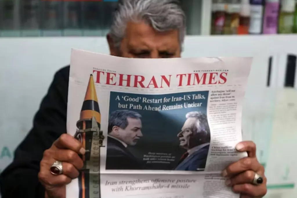 A person holding a Tehran Times newspaper featuring a headline about Iran-US talks and an image of a missile.