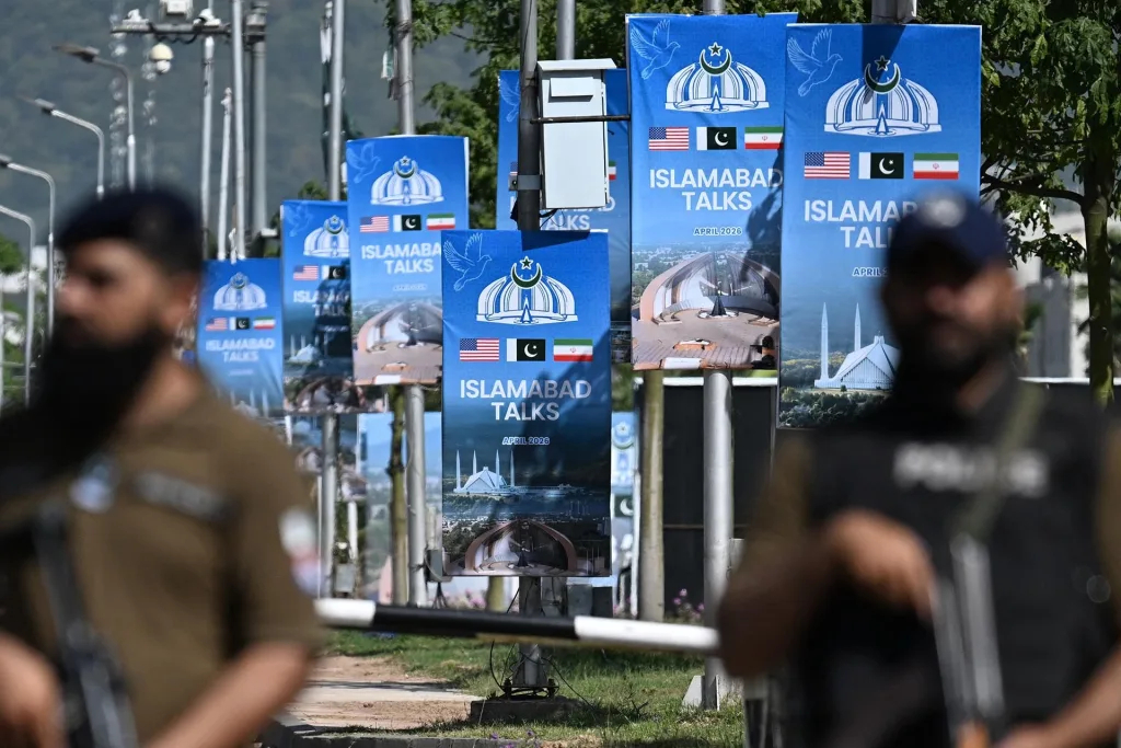 A row of blue banners on a street promoting "Islamabad Talks" for April 2026, featuring flags of the USA, Pakistan, and Iran.