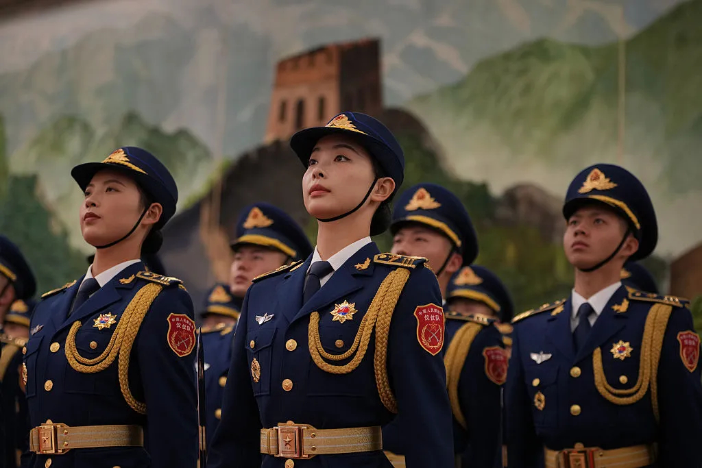 Chinese female and male military officers in blue dress uniforms standing in formation with the Great Wall of China in the background.