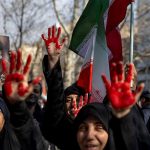 Iranian protesters in a crowd with red-painted palms raised and a portrait of Ali Khamenei.