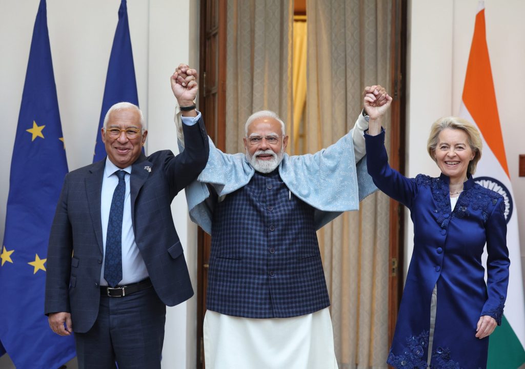 Indian Prime Minister Narendra Modi standing between two European leaders, holding their hands up in a gesture of unity.