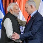 Indian Prime Minister Narendra Modi and Israeli Prime Minister Benjamin Netanyahu shaking hands in front of national flags.