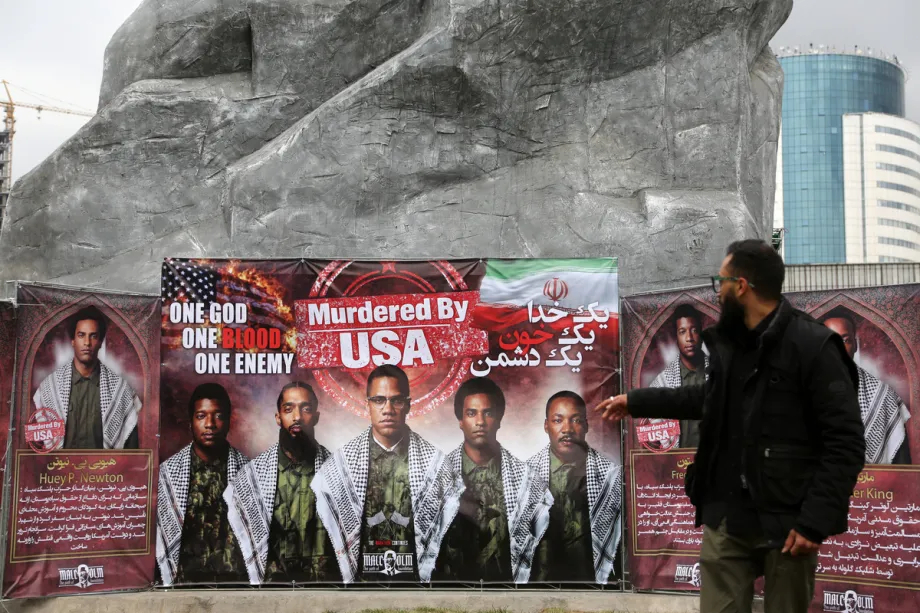 A large outdoor banner in Iran featuring various historical figures and the text "Murdered By USA" in English and Persian.