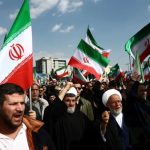 A large crowd of people in Iran waving Iranian flags and chanting during a demonstration.