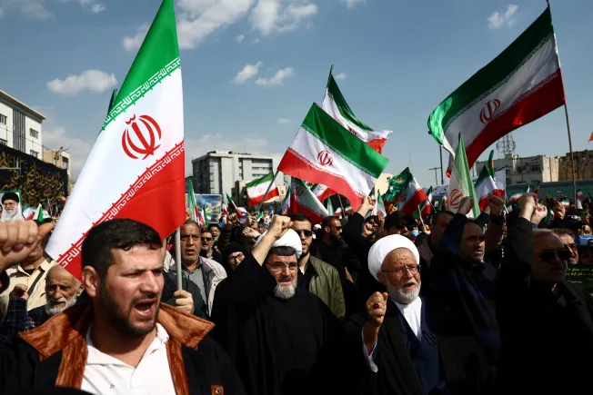 A large crowd of people in Iran waving Iranian flags and chanting during a demonstration.