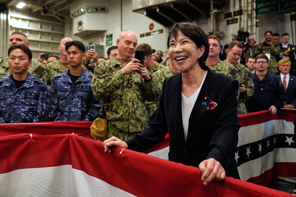 A high-ranking Japanese official smiling and engaging with military personnel on a naval vessel decorated with flags.