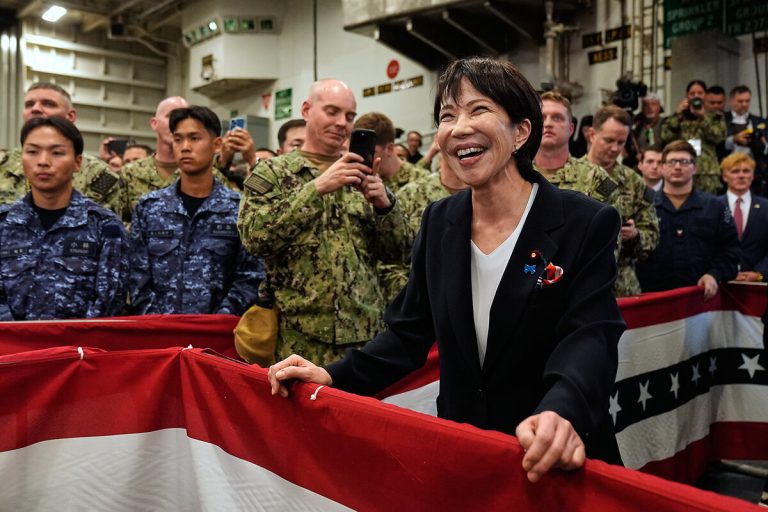 A high-ranking Japanese official smiling and engaging with military personnel on a naval vessel decorated with flags.