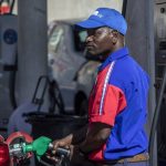 A man in a blue and red uniform refueling a car at a gas station in Africa.