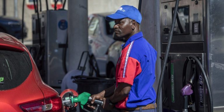 A man in a blue and red uniform refueling a car at a gas station in Africa.