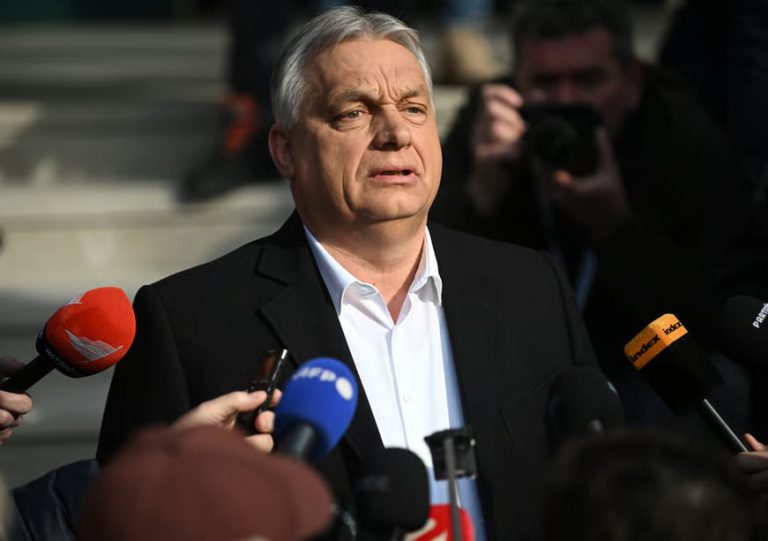 Viktor Orbán speaking to a crowd of journalists with several microphones in the foreground.