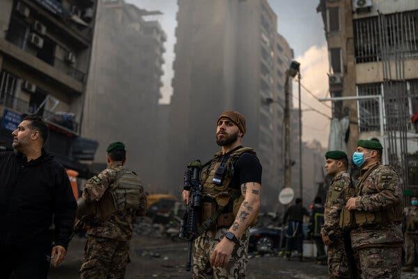 Soldiers in military gear standing in a war-torn urban street with smoke in the background.