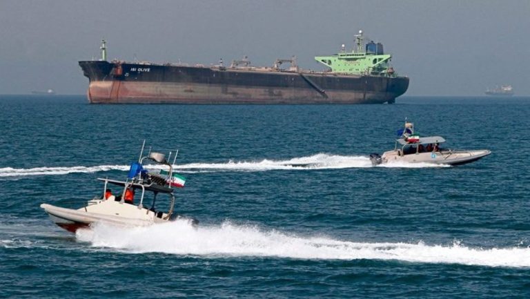 Two Iranian military speedboats patrolling near a large cargo ship or oil tanker at sea.