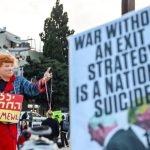 Protesters in an urban setting holding a sign that reads "War without an exit strategy is a national suicide!"