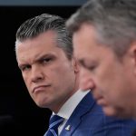A close-up of a serious-looking official in a blue suit during a formal meeting.