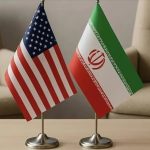 Small table flags of the United States and Iran placed side by side on a wooden table.