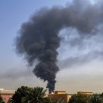 Large plume of thick black smoke rising from a building in a Middle Eastern urban area.