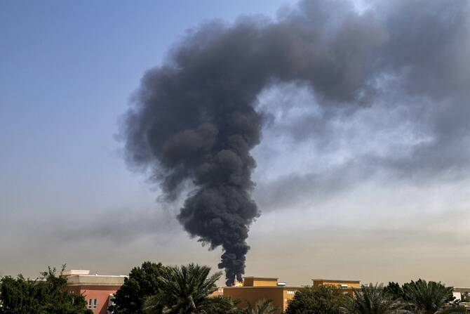 Large plume of thick black smoke rising from a building in a Middle Eastern urban area.