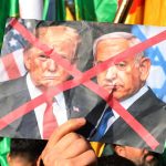 A protester holding a crumpled photo of Donald Trump and Benjamin Netanyahu with a red 'X' over it.