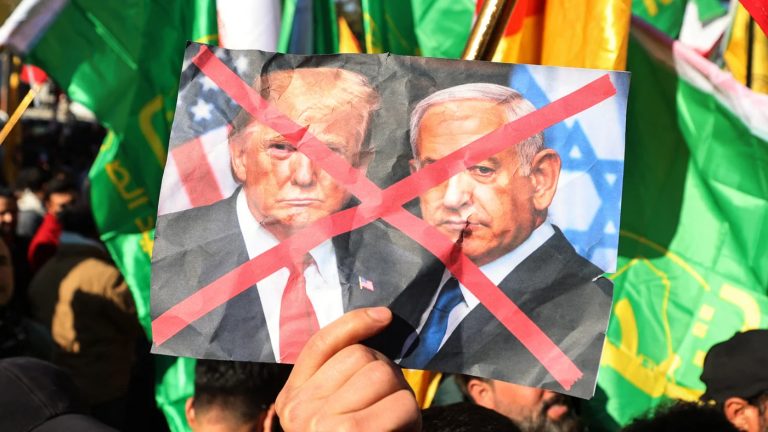 A protester holding a crumpled photo of Donald Trump and Benjamin Netanyahu with a red 'X' over it.