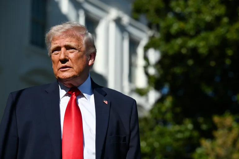 Donald Trump standing outdoors in a suit and red tie with the White House in the background.