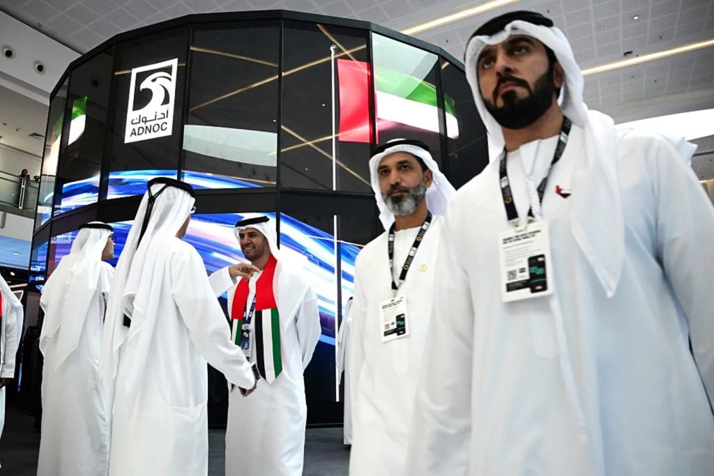 Men in traditional Emirati clothing walking in front of a large ADNOC logo.