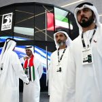 Men in traditional Emirati clothing walking in front of a large ADNOC logo.