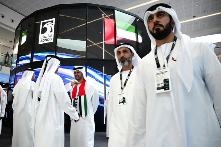 Men in traditional Emirati clothing walking in front of a large ADNOC logo.