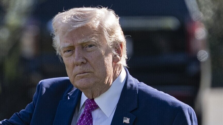 A portrait of Donald Trump looking directly at the camera with a serious expression, wearing a blue suit and purple tie.