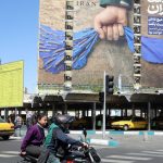 A street scene in Tehran featuring a large political billboard showing a hand controlling the Strait of Hormuz.