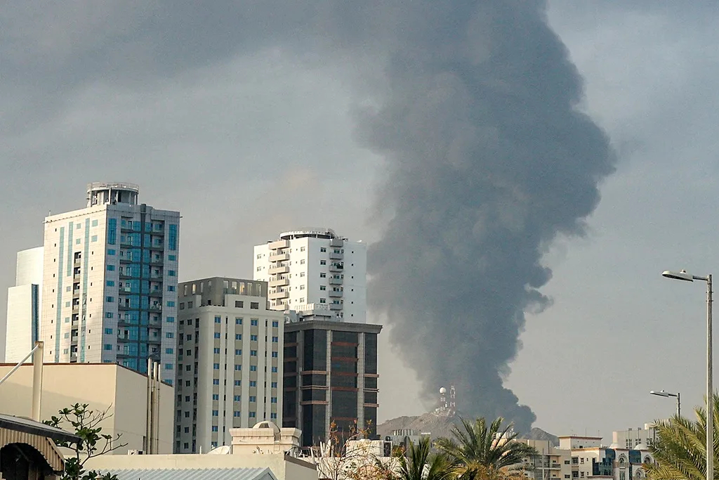 Large plumes of dark gray smoke rising behind urban apartment buildings under an overcast sky.