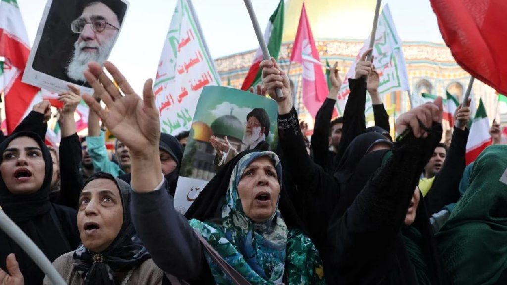 A crowd of Iranian women in black chadors protesting and holding portraits of Ayatollah Khamenei and Iranian flags.