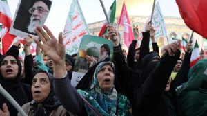 A crowd of Iranian women in black chadors protesting and holding portraits of Ayatollah Khamenei and Iranian flags.