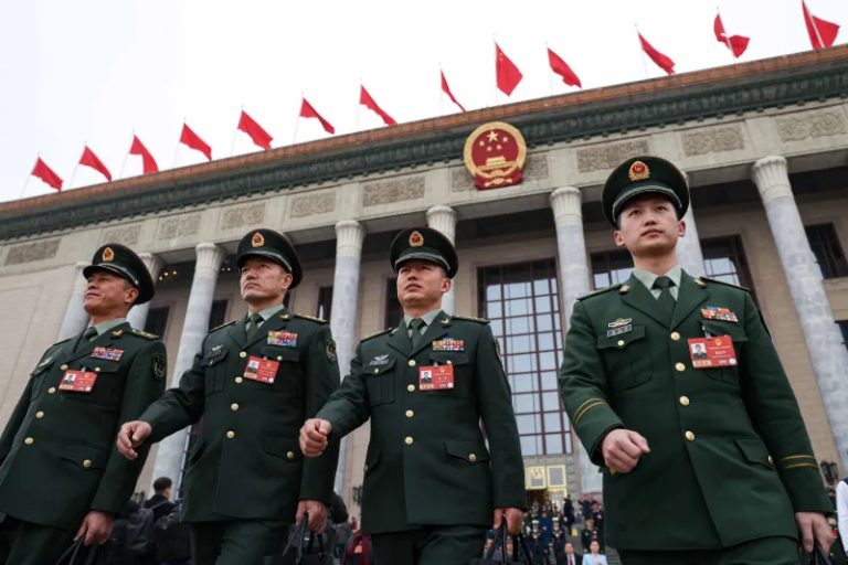 Chinese military officers in green uniforms walking in front of the Great Hall of the People in Beijing.