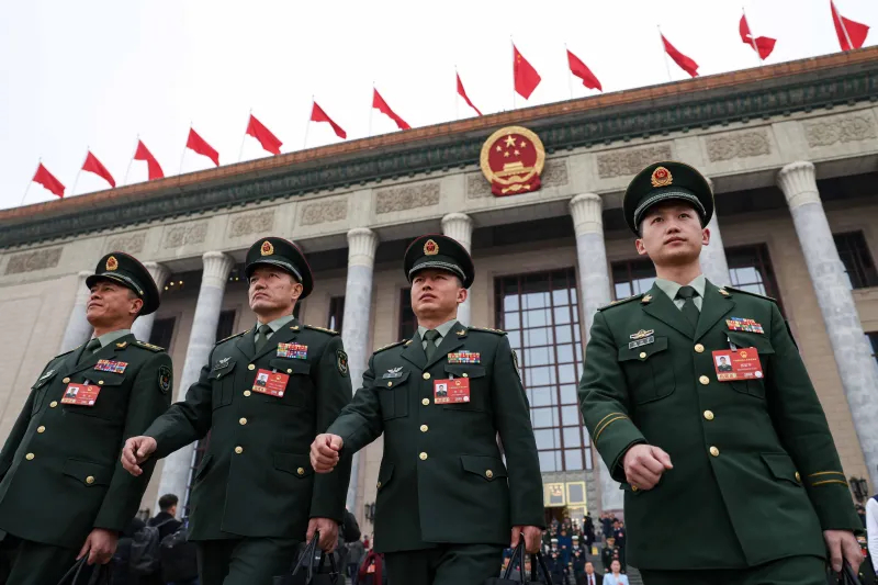 Chinese military officers in green uniforms walking in front of the Great Hall of the People in Beijing.
