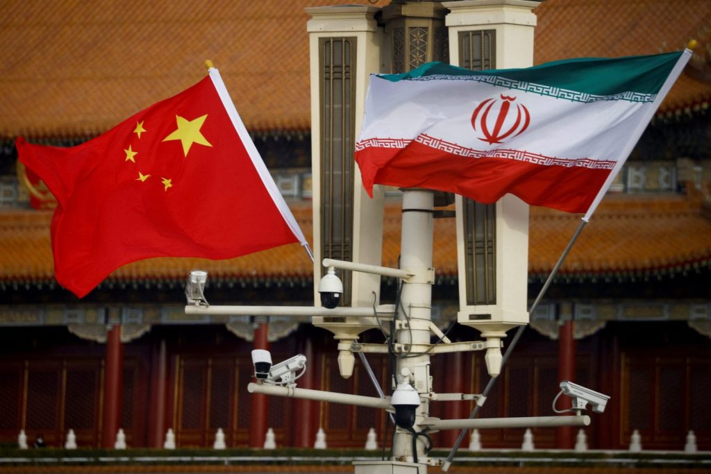The national flags of China and Iran flying together on a lamp post in front of a traditional Chinese building.