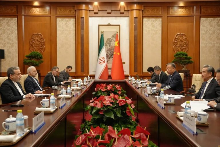 Official diplomatic meeting between Iranian and Chinese delegations seated at a long conference table with national flags.