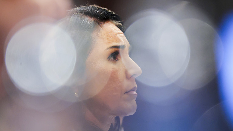Close-up profile shot of Tulsi Gabbard with soft-focus bokeh lighting in the background.