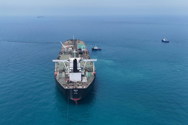 : Large oil tanker Helga being escorted by tugboats in open blue water.
