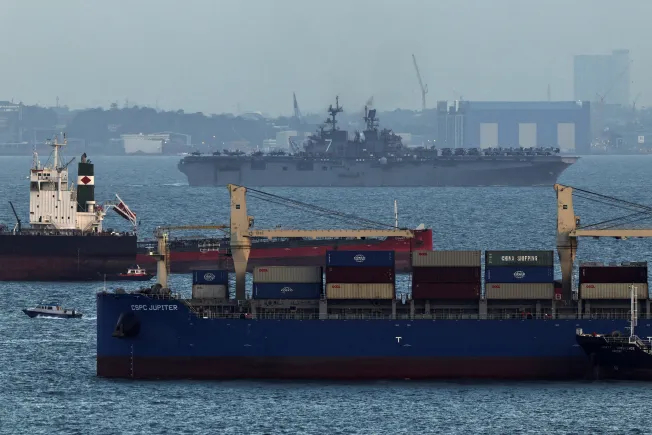 A U.S. Navy warship sailing past commercial cargo container ships in a maritime chokepoint.