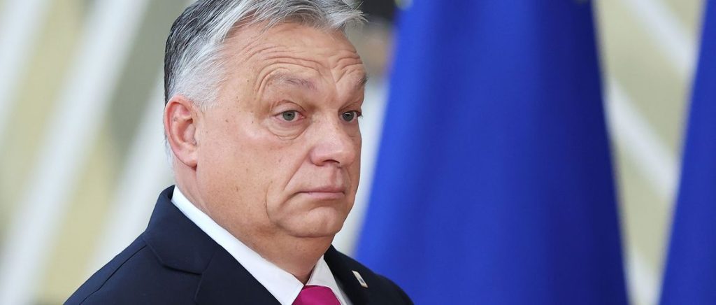 Close-up portrait of Hungarian Prime Minister Viktor Orbán against a blurred background of European Union flags.