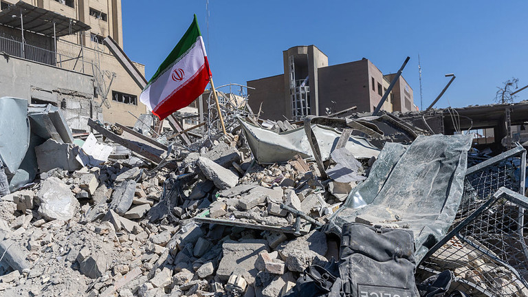 The Iranian flag flying over a pile of concrete rubble and destroyed buildings.