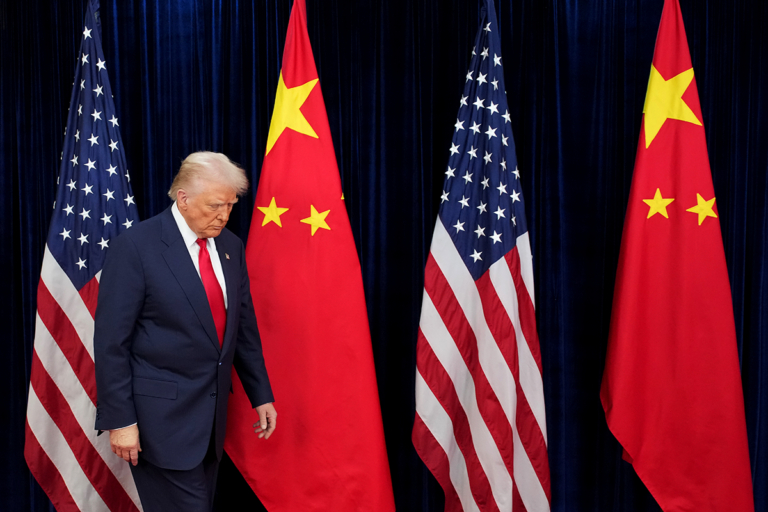 Donald Trump walking past American and Chinese flags with a somber expression.