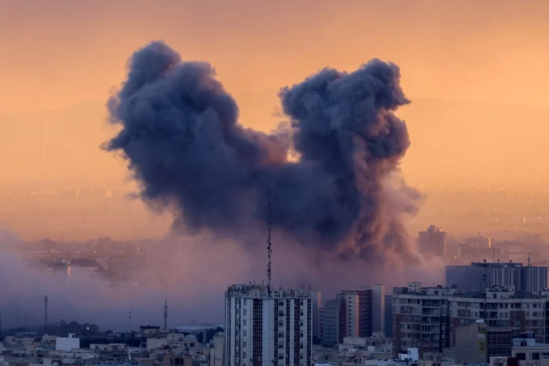 Thick smoke clouds rise over an urban landscape following military strikes.