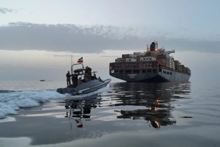 Military speedboat approaching a large container ship at dusk.
