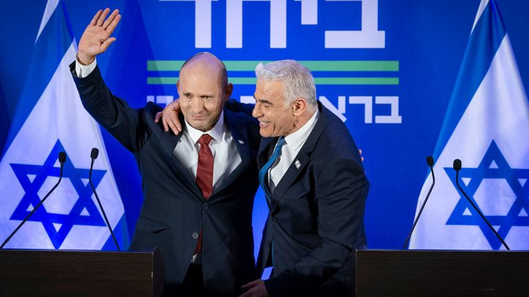 Naftali Bennett and Yair Lapid standing together at a podium with Israeli flags.