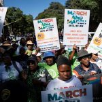 A crowd of demonstrators holding up protest signs reading March and March against illegal immigration and crime.